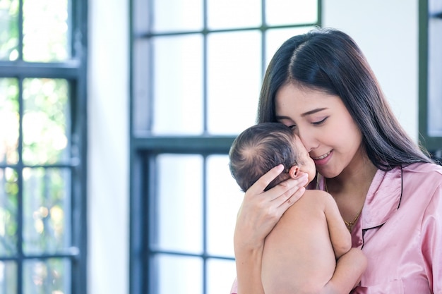 Een Toddler baby in een tedere omhelzing van moeder bij het raam