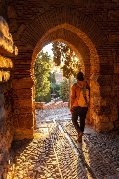 Een toerist die in de zonsondergang loopt bij de poort van de Alcazaba-muur in de stad Malaga, Andalusië. Spanje. Middeleeuws fort in Arabische stijl