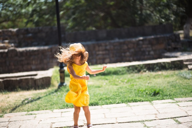 Een toeristisch meisje met een gele hoed en een zomerjurk die danst langs de straat van de oude stad, gemaakt van steen met een fort Sightseeing-tour