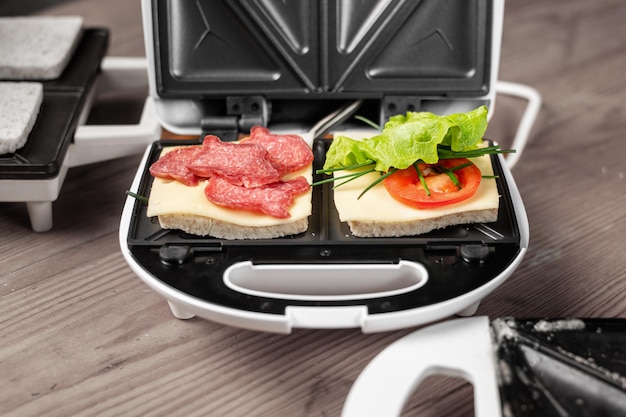 Een tosti-ijzer met twee verschillende sandwiches met tomaten ham uien en kaas Het bereiden van een lichte maaltijd