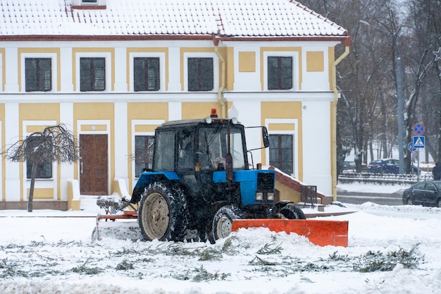 Een tractor maakt sneeuw in de stad schoon in de winter na een sneeuwval Stadsstraten schoonmaken van sneeuw Tractorchauffeur aan het werk op het stadsplein tijdens een sneeuwstorm