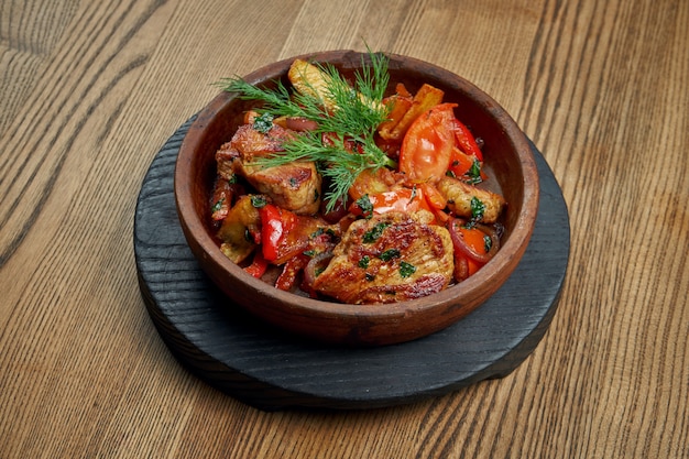 Een traditioneel gerecht uit de Georgische keuken - gestoofde ojahuri met aardappelen, lamsvlees, tomaten en kruiden in een keramische kom op een houten oppervlak