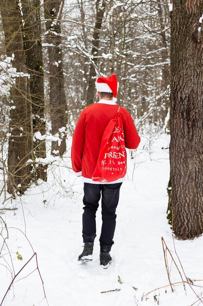 Een traditionele kerstman met een hoed en een zak geschenken loopt door het bos met geschenken. Achteraanzicht.