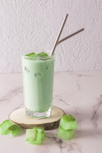 Een transparant hoog glas met biologische koude groene matcha-thee en ijsblokjes met milieuvriendelijk metalen rietje op een houten natuurlijk podium vooraanzicht