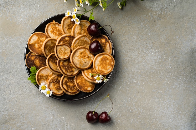 Een trendy huisgemaakt ontbijt met kleine pannenkoeken close-up. Mini pannenkoeken, kersen, thee op tafel. Horizontale oriëntatie