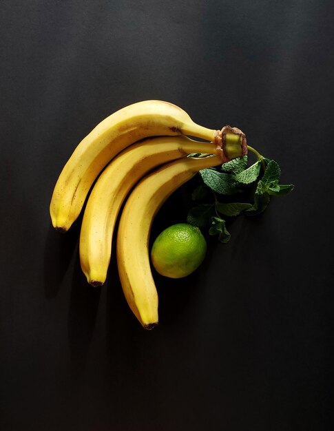 Een tros bananen een takje munt en limoen op een donkere achtergrond