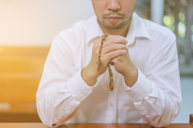 Een trouwe Aziatische jonge man dient een gebedsgebaar in dat alleen op de bank in de kerk zit te bidden