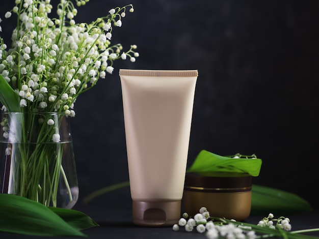 Een tube gezichts- en huidcrème op een zwarte tafel met een boeket van lelietje-van-dalenbloemen