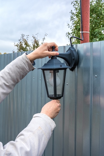 Een tuinman installeert een straatlantaarn op een metalen hek huishoudelijk werk in de tuin