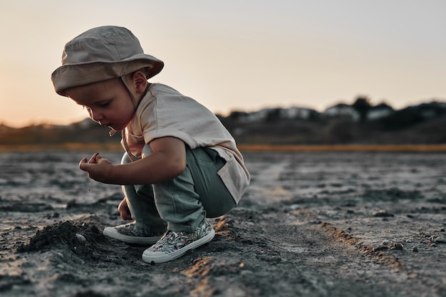 Een tweejarig kind met een gehurkt hoed raakt iets op een landweggetje aan