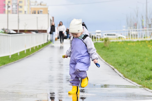 Een tweejarig meisje met rubberen laarzen springt door plassen Bewolkt weer