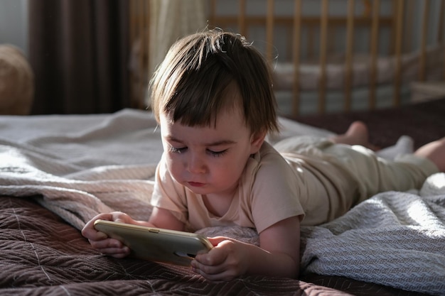 Een tweejarige jongen ligt op een bed en kijkt tekenfilms op een smartphone