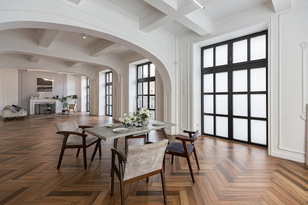 een uitzicht op een set eettafel in een chique dure heldere interieur van een enorme woonkamer in een historisch herenhuis met gebogen bogen kolommen en witte muren versierd met ornamenten en stucwerk