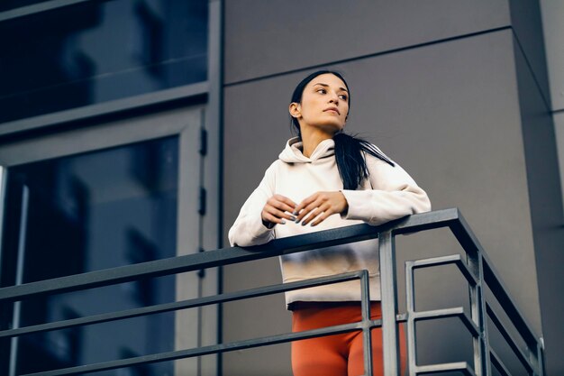 Een urban sportvrouw in sportkleding kijkt rond terwijl ze leunt op de reling