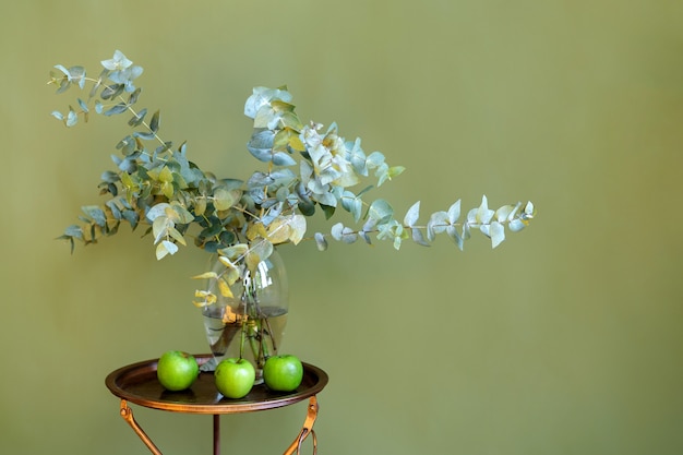 Een vaas met bloemen en groene appels op tafel, op een groene achtergrond