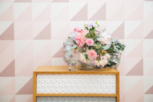 Een vaas met bloemen op een ladekast bij de muur met een geometrisch patroon in een lichtroze woonkamer