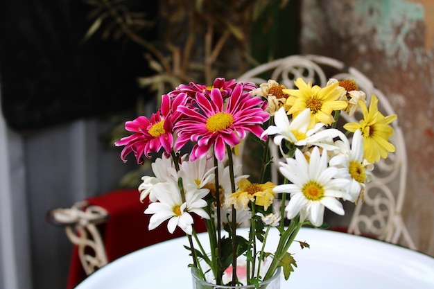 Een vaas met bloemen staat op een tafel met een stoel op de achtergrond.