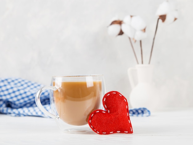 Een vaas met katoen, rood hart, koffie in de ochtend tegen een lichte muur, concept, een ansichtkaart voor Valentijnsdag.