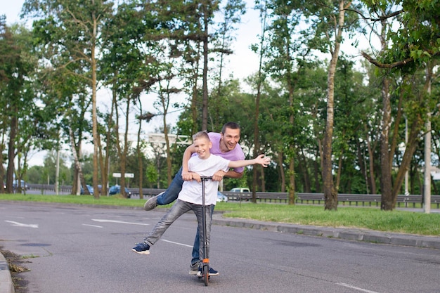 Een vader berijdt zijn zoon in een wit T-shirt op een scooter, het gelukkige kind spreidde zijn handen