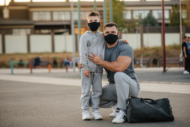 Een vader en kind staan in maskers op een sportveld na een training tijdens zonsondergang.