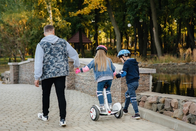 Een vader helpt en leert zijn jonge kinderen om tijdens zonsondergang op een Segway in het park te rijden