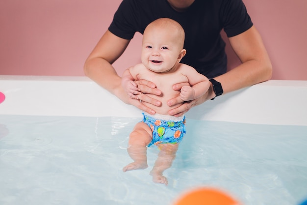 Een vader helpt zijn babyjongen tijdens zwemlessen in het zwembad.