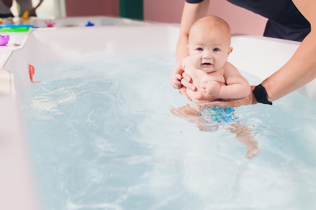 Een vader helpt zijn babyjongen tijdens zwemlessen in het zwembad.