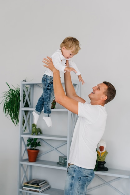 Een vader knuffelt gooit in de lucht zijn zoon in zijn armen houdt hem vast. gekleed in jeans en witte t-shirts in een licht interieur.