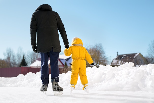 Een vader leert zijn dochter schaatsen thuis op zijn eigen ijsbaan terwijl hij haar hand vasthoudt