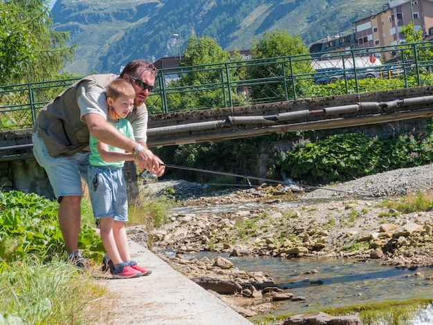 een vader leert zijn zoontje vissen bij de rivier op de berg