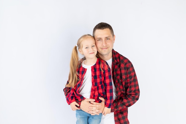 Een vader met een dochtertje op een witte geïsoleerde lege achtergrond in een fotostudio in rode shirts die knuffelend speelt Gelukkig vaderschap of gezin