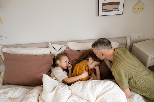Een vader steekt zijn twee dochters, die al diep in bed slapen, liefdevol in bed