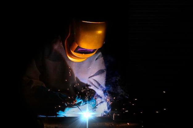 Een vakman is aan het lassen met werkstukstaal. Werknemer Over lasserstaal Elektrisch lasapparaat gebruiken Er komen lichtlijnen naar buiten en veiligheidsuitrusting in de fabrieksindustrie.