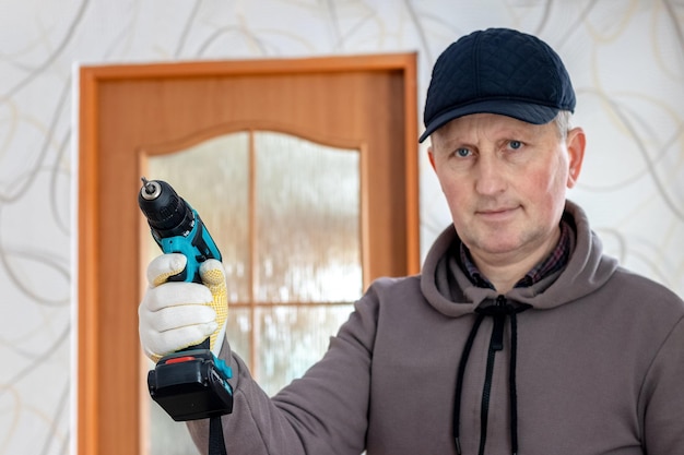 Een vakman met een draadloze schroevendraaier in zijn hand in een kamer bij de deur