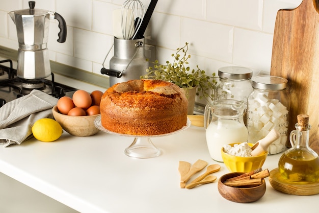 Een vanillecake en ingrediënten op een caketribune op het aanrecht in de keuken