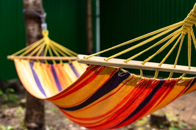 Een veelkleurige stoffen hangmat hangt in de bomen in de zonnestralen in de open lucht