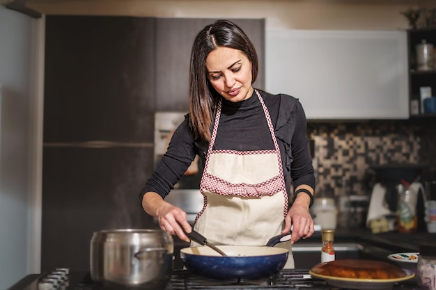 Een veertigjarige vrouw kookt in haar eigen keuken en roert de saus in de pan op het fornuis