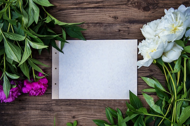 Een vel papier en een paar witte en roze pioenrozen op hout met kopie ruimte als een briefkaart