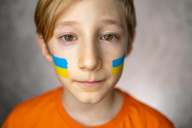 Een verdrietig kind tegen de oorlog een jongen met tranen in zijn ogen en een geschilderde vlag van Oekraïne op zijn wangen kijkt met medelijden naar de camera