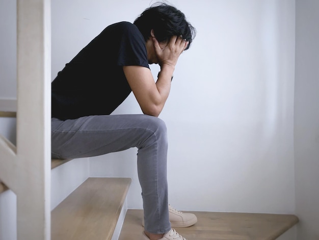 Een verdrietige man zit met zijn handen bedekt zijn gezicht op de trap bij het raam angst en depressie