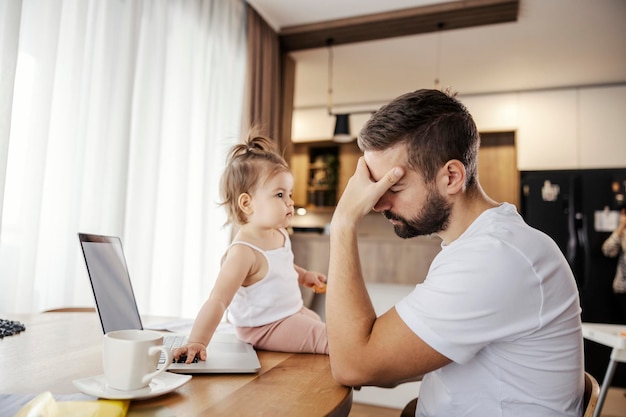 Een verdrietige vader zit thuis en werkt op afstand terwijl zijn dochter zijn werk verpest