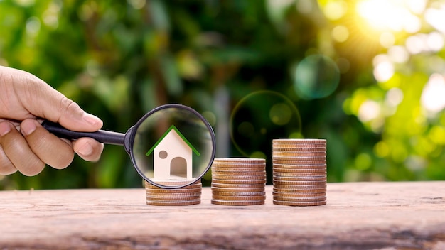 Foto een vergrootglas en een modelhuis op een stapel munten besparingsconcepten en financiële plannen voor investeringen in woningen