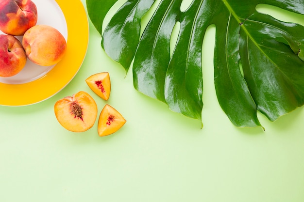 Een verhoogde weergave van perzik fruit met monstera groen blad op pastel achtergrond