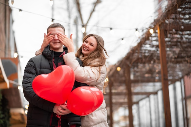 Een verliefd meisje op straat zorgt voor een verrassing voor een man. Een man houdt hartvormige ballonnen in zijn handen. Valentijnsdag concept, geschenken, liefde, winkelen