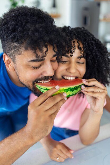 Een verliefd paar eet een zoete watermeloen in de keuken Een man en een vrouw eten een rijpe watermeloen in de keuken Gelukkig paar dat watermeloen eet Portret van een paar met een watermeloen