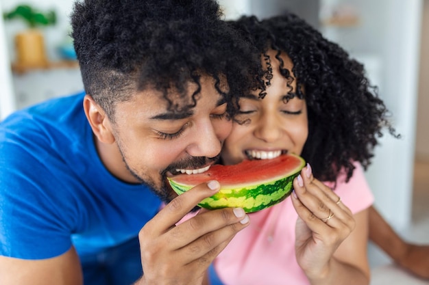 Een verliefd paar eet een zoete watermeloen in de keuken Een man en een vrouw eten een rijpe watermeloen in de keuken Gelukkig paar dat watermeloen eet Portret van een paar met een watermeloen