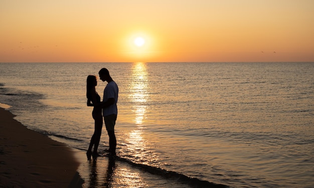 Foto een verliefd stel beleeft romantische tedere momenten bij zonsondergang op het strand jonge geliefden op zomervakantie concept van liefde of huwelijksreis kus in silhouet bij zonsondergang kopie ruimte