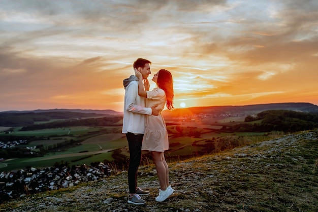 Een verliefd stel, een jongen en een meisje staan bij zonsondergang op een berg te knuffelen en te zoenen