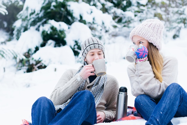 Een verliefd stel in warme kleren zit in de sneeuw en drinkt uit bekers