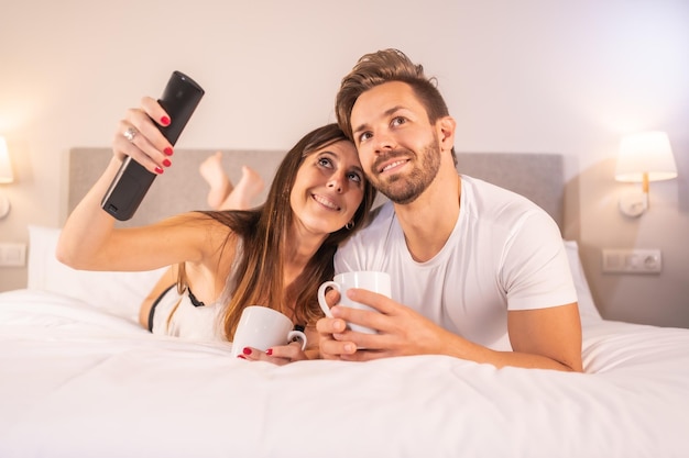 Een verliefd stel kijkt tv op het hotelbed in pyjama